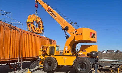 A Broderson RT-400 Crane uses its boom and winch to carefully lift a large industrial component next to a shipping container