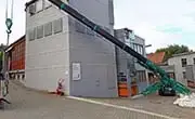 Maeda MC815C spider crane operating with extended boom alongside a building exterior