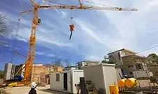 Potain Hup M 28-22 A self-erecting crane lifting a concrete bucket over an active jobsite.