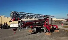 Potain self-erecting tower crane staged on outriggers with timber mats, with the jib folded out and a technician preparing the unit for setup and lifting.